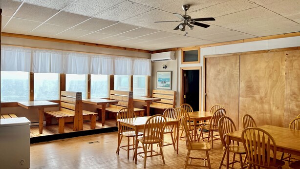 A restaurant with wooden furniture, a ceiling fan, and a view of the city. - Bennett Lodge (Daniel's Harbour)