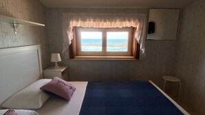 A bedroom with a bed, a nightstand, a window with a view of the sea, and a small stool. - Casa Mare Holiday, Beachfront villa equipped with amenities and beach nearby (Sicilia)