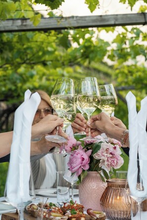 Un groupe de personnes trinquant avec des verres de vin autour d’une table en plein air, agrémentée d’un arrangement floral et d’un chandelier.