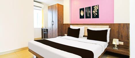 A modern hotel room with a large bed, a wardrobe, a bedside table with a lamp, and a wall with three framed pictures.