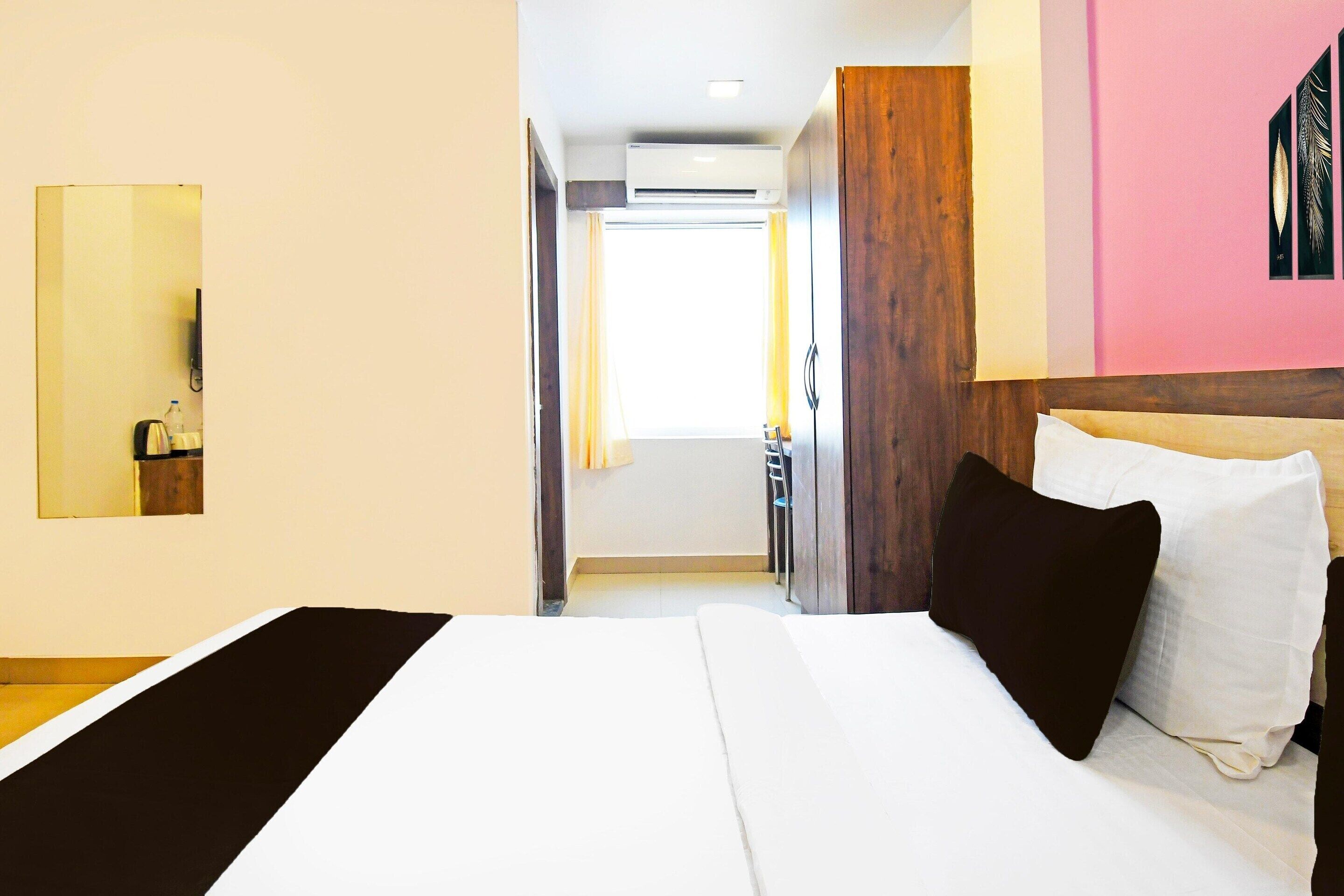 A hotel room with a bed, a mirror, a wooden headboard, a door leading to a bathroom, and a wall-mounted air conditioning unit.
