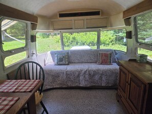A cozy interior with a sofa bed, a dining table, and a cabinet. - Vintage Airstream Excella in a Private Setting - Avail. May 15 through Oct. 31 (Penobscot)