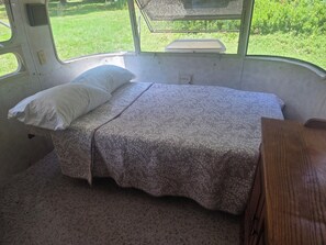 A small, enclosed sleeping area with a bed, a pillow, and a bench. - Vintage Airstream Excella in a Private Setting - Avail. May 15 through Oct. 31 (Penobscot)