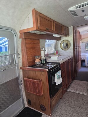A compact kitchen with wooden cabinets, a stove, and a sink. - Vintage Airstream Excella in a Private Setting - Avail. May 15 through Oct. 31 (Penobscot)