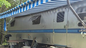 Une caravane ancienne dotée d’un auvent rayé, d’une table et d’une chaise.