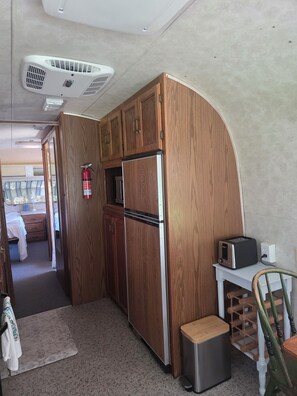 A compact kitchen with wooden cabinets, a stainless steel refrigerator, a microwave, and a toaster. - Vintage Airstream Excella in a Private Setting - Avail. May 15 through Oct. 31 (Penobscot)