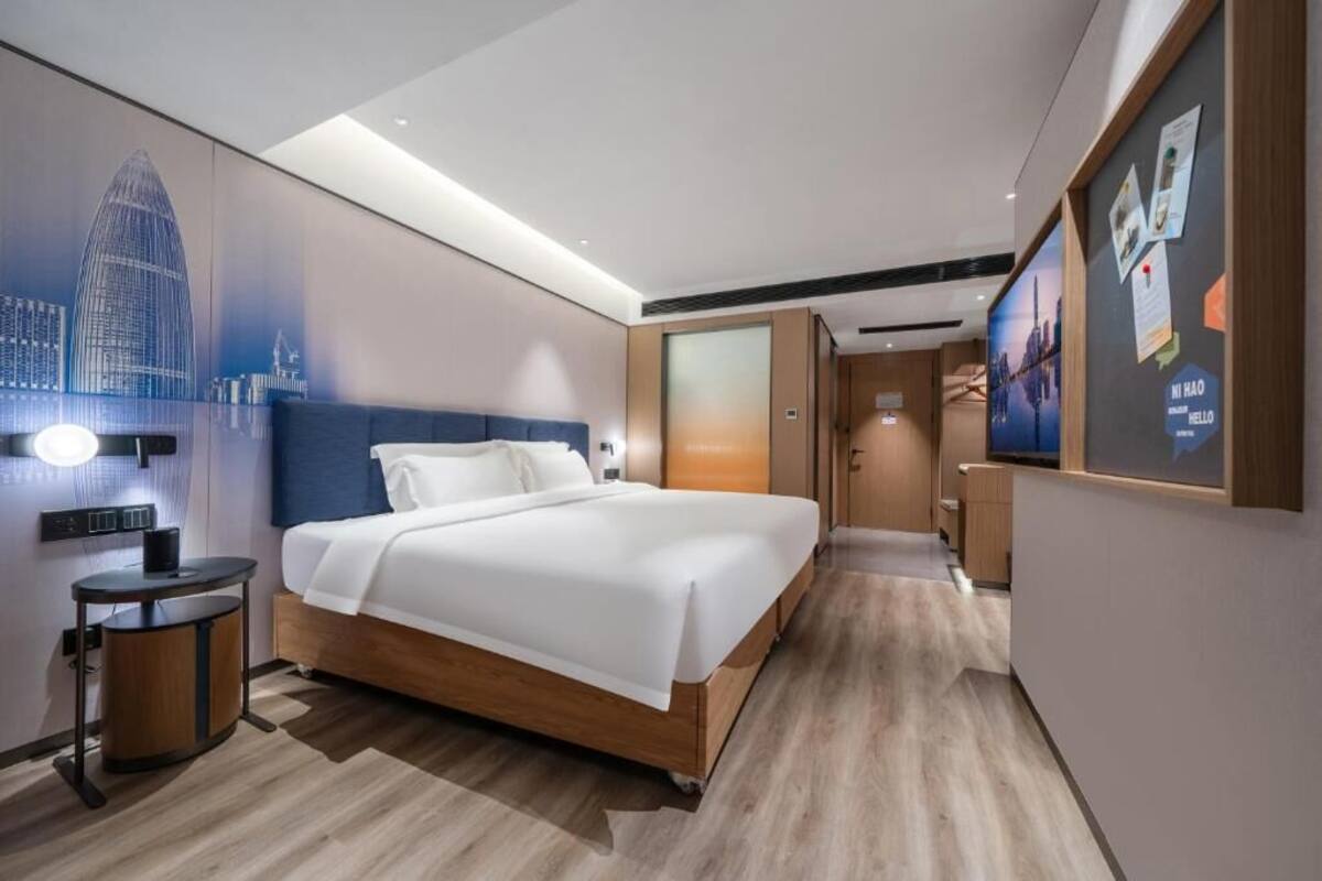 A modern hotel room with a large bed, a bedside table, a wall-mounted TV, and a cityscape mural.
