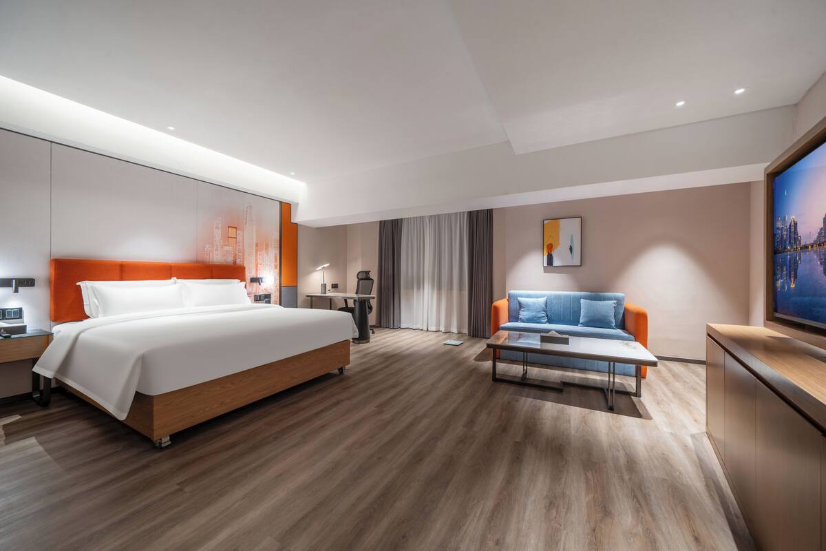 A modern hotel room with a large bed, a sofa, a desk, and a TV.