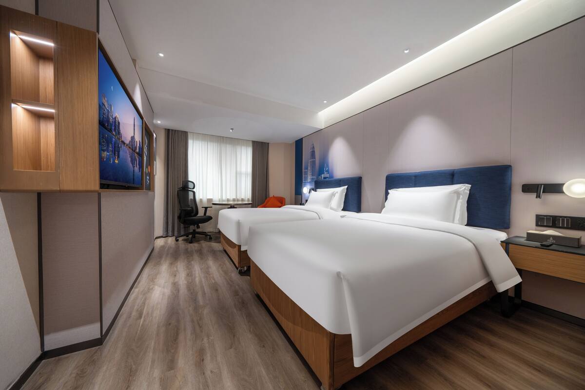 A hotel room with a large bed, a desk, a chair, and a television on the wall.