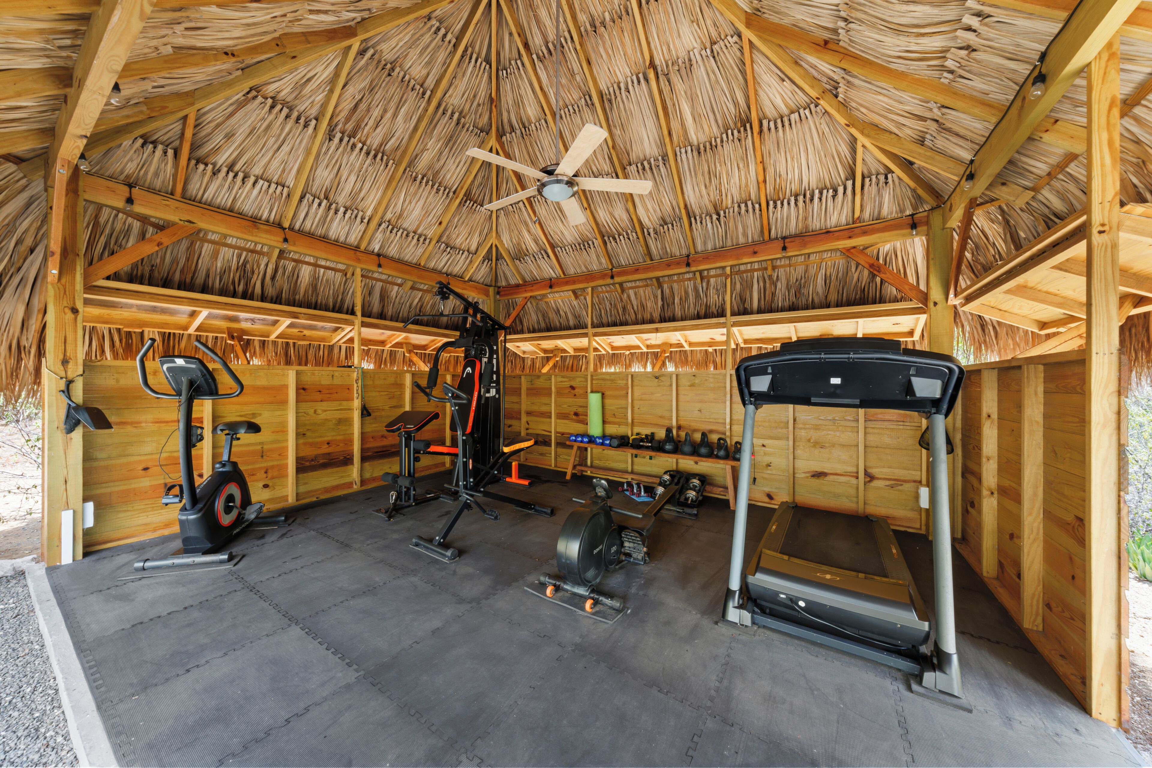 Une salle de sport couverte, équipée de matériel d’exercice, dotée d’un ventilateur de plafond et d’une structure en bois.