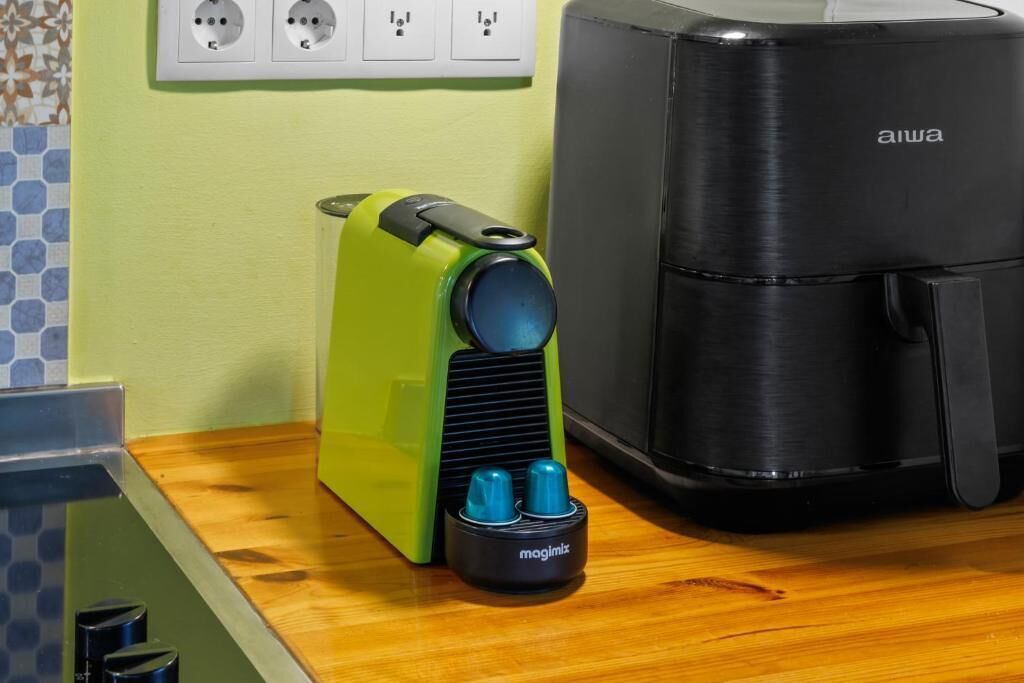 A kitchen with a green appliance, a black air fryer, and a power outlet with three sockets.