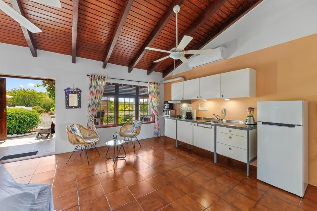 A kitchen with a ceiling fan, white cabinets, a refrigerator, and a dining area with chairs.