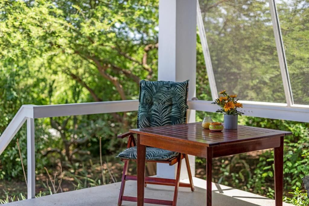 Un tavolo in legno con una sedia, un vaso con fiori e vista sul verde attraverso una finestra.