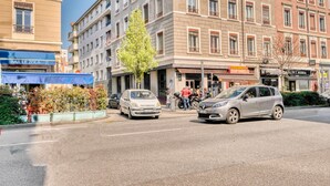 Une vue d’une rue, avec des voitures garées le long du trottoir, un bâtiment portant une enseigne indiquant « BAR LE ZOLA », et une autre enseigne indiquant « A. C. CORONERIE TOP’S SMELLIES ».