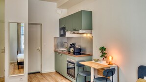 Une cuisine compacte équipée d’une cuisinière, d’un four et d’un évier, un petit coin repas avec une table et des chaises, et un miroir sur le mur de gauche.