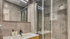 Une salle de bain moderne avec une douche à l’italienne, un lavabo blanc avec un meuble-vasque en bois et un grand miroir au-dessus du meuble-vasque.