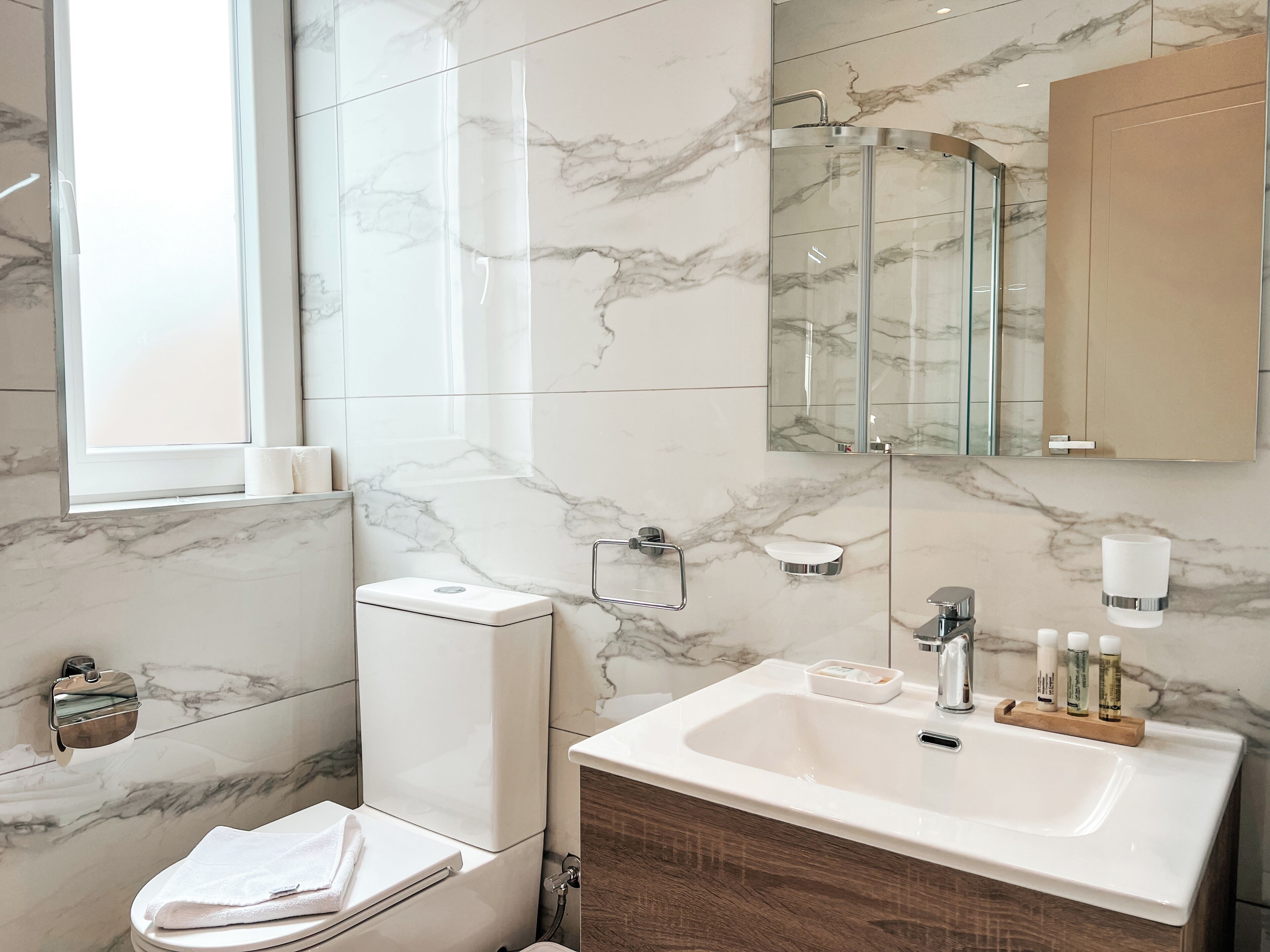 A modern bathroom with a marble floor, a toilet, a sink with a vanity, a glass shower enclosure, and a large mirror.