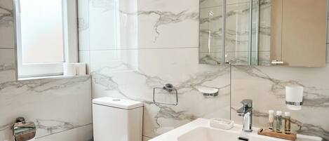 A modern bathroom with a marble floor, a toilet, a sink with a vanity, a glass shower enclosure, and a large mirror.