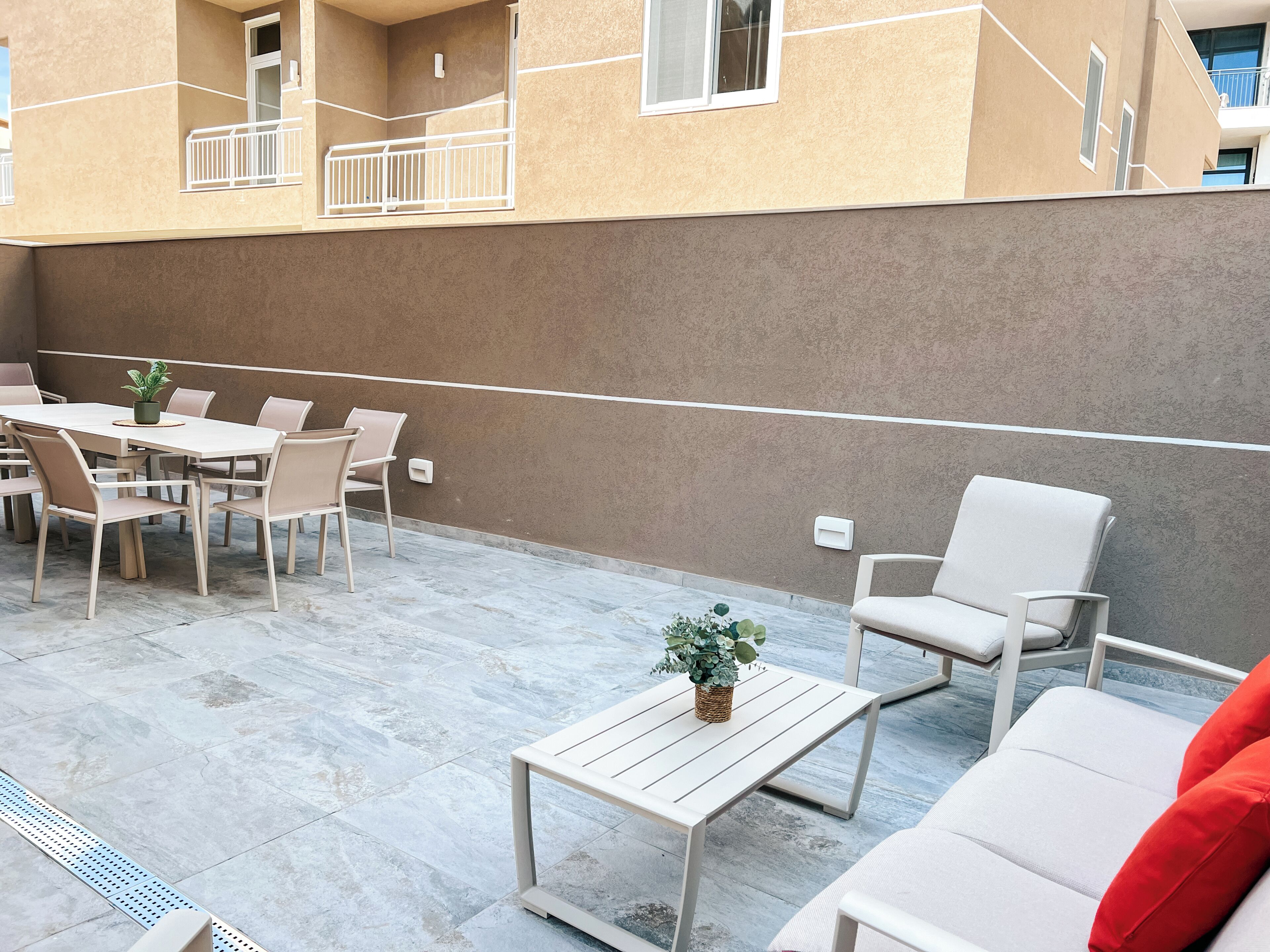 Un patio al aire libre con una mesa, sillas, una planta pequeña y un sofá con un cojín rojo.