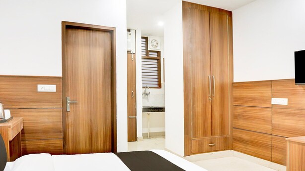 A bedroom with a bed, wooden wardrobe, and a television. - Deluxe Cybercity U19 (Gurugram)