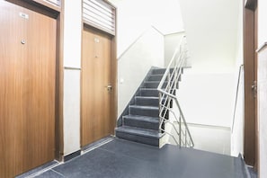 Un pasillo con dos puertas de madera, una escalera con barandillas metálicas y un suelo de baldosas.