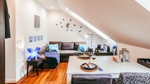 Moderni loft-tyylinen huoneisto, jossa on parvelle sijoitettu sänky, ruokailutila kahdelle katetulla pöydällä, sohva ja pieni keittiö.