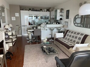 A modern living room with a sofa, coffee table, and a dining area with a kitchen in the background. - SUPERB WATERFRONT SEA/MOUNTAIN APARTMENT. EXCEPTIONAL SEA VIEW! (Saint-Raphaël)