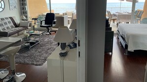 Moderni hotellihuone, jossa on suuri ikkuna, josta avautuu näkymä merelle, sohva, ruokailutila ja sänky.