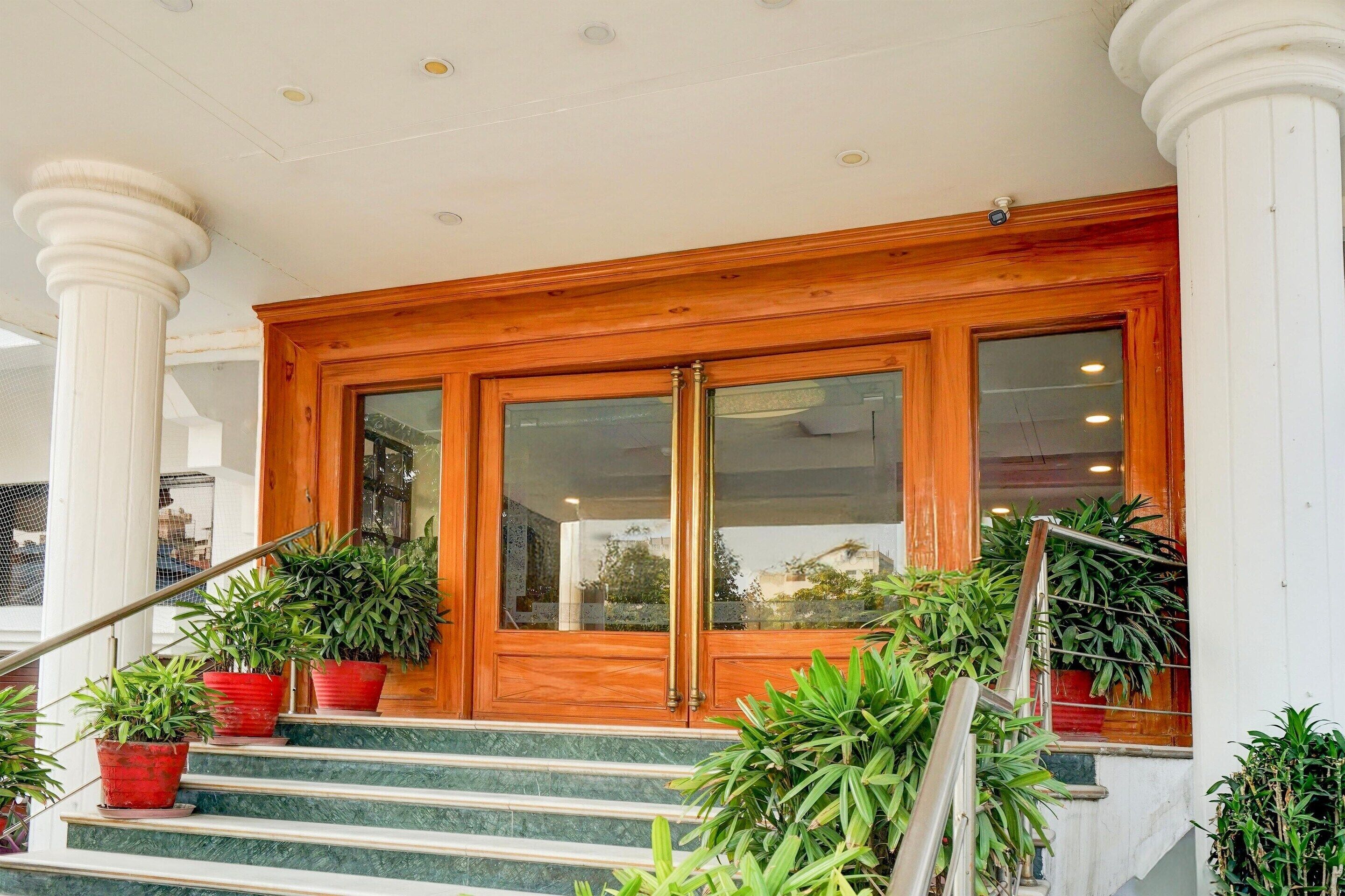 A wooden double door entrance with glass panels, a marble staircase, and potted plants.