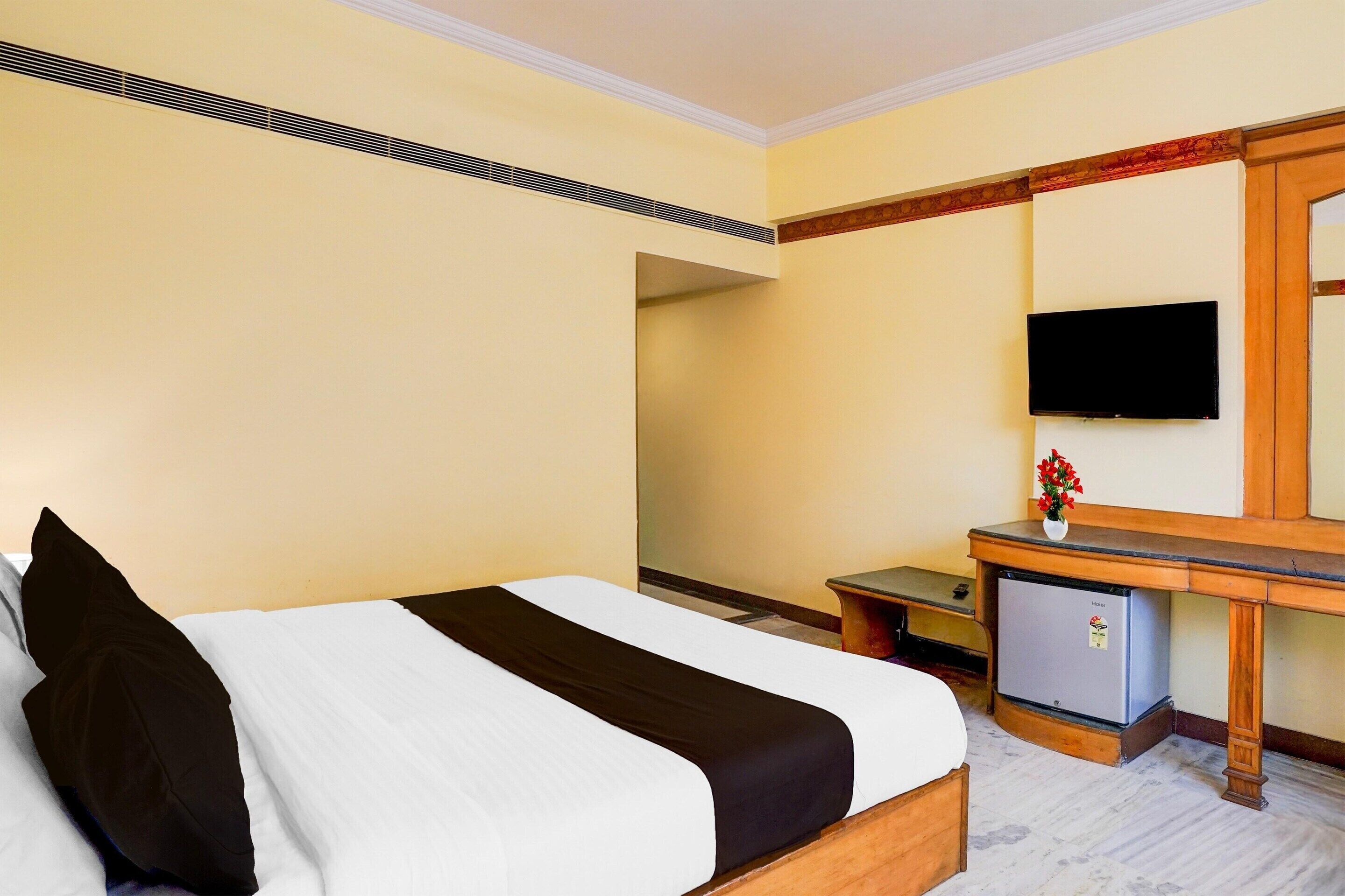 Una habitación de hotel con cama, escritorio, televisor y un refrigerador pequeño.