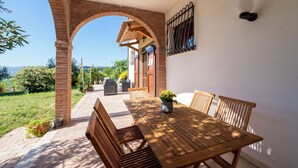 Um pátio com mesa e cadeiras de madeira, um arco de tijolos e vista para o campo.