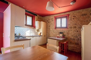 A kitchen with a wooden table, chairs, a stove, and a stone wall. - Bright apartment in farmhouse with pool and view of Assisi (Umbria)