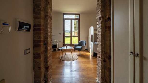 Um quarto com um arco de tijolos, uma mesa redonda com um tapete, uma cadeira azul e uma porta com puxador.