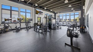 Une salle de sport équipée de divers appareils d’exercice, dotée de grandes fenêtres et d’un plafond haut.