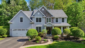 A two-story house with a garage, a stone accent wall, and a well-manicured front yard with trimmed bushes. - NEW Luxury Saratoga Track Rental: 4 miles to track, Hot tub, Sunroom, 8 beds! (Saratoga Springs)