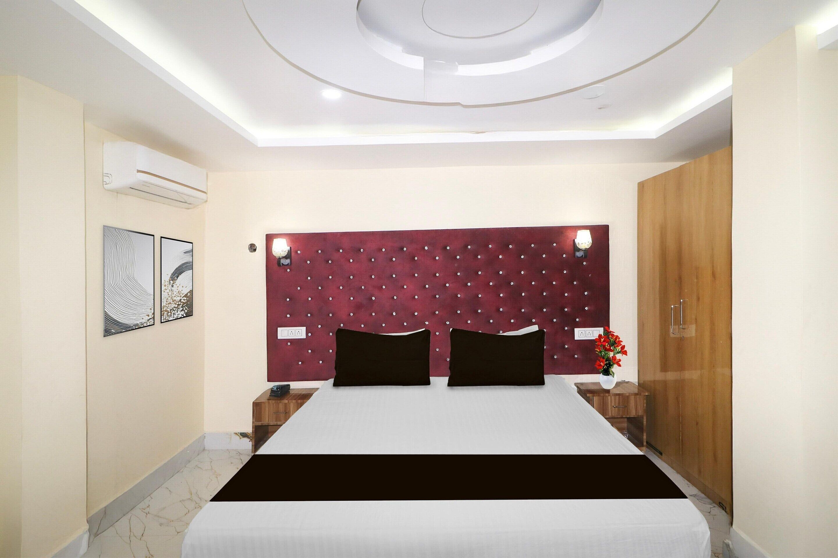 A hotel room with a bed, a headboard with lights, a wooden wardrobe, and a wall-mounted air conditioner.