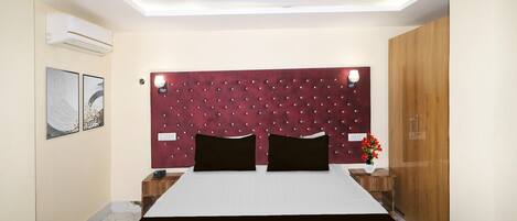 A hotel room with a bed, a headboard, a nightstand, a wardrobe, and a wall-mounted air conditioner.