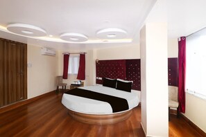 A bedroom with a bed, wooden flooring, a ceiling with recessed lighting, a wardrobe, and a window with curtains. - Super Deluxe Room Hotel Rise And Dine (Dhanbad)