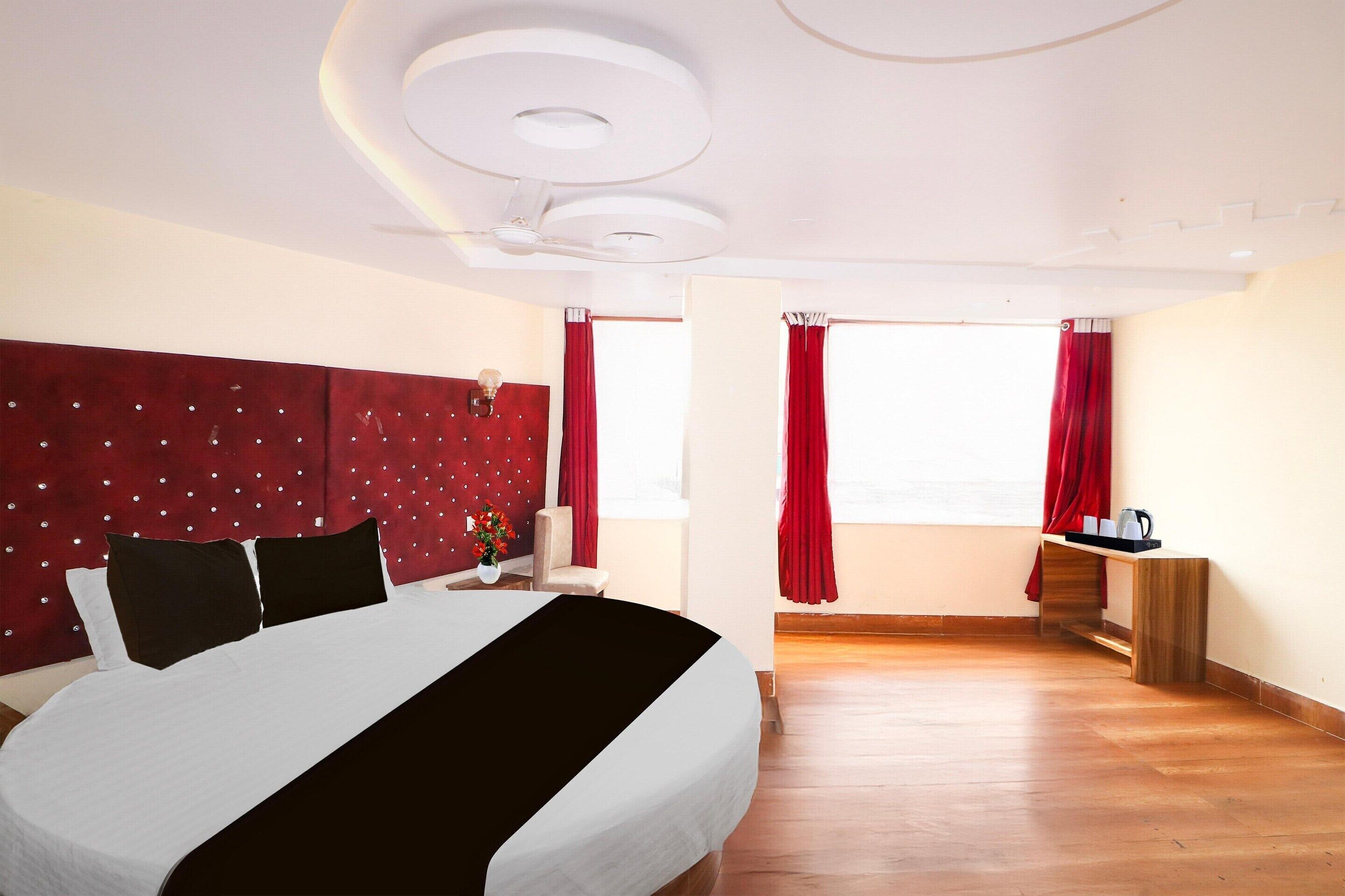 A hotel room with a bed, a desk, a chair, a window with curtains, and a ceiling light fixture.