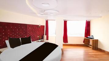 A hotel room with a bed, a desk, a chair, a window with curtains, and a ceiling light fixture.