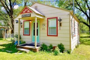 A small, single-story house with a porch, a welcome sign, and a mailbox.