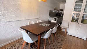 Uma sala de jantar com mesa de madeira, cadeiras brancas, tapete estampado e luminária pendente.