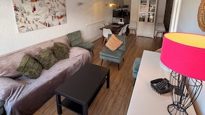 Sala de estar com sofá, cadeiras, mesa de centro, luminária e cozinha ao fundo.