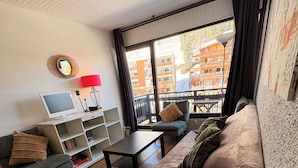 Sala de estar com sofá, poltrona, televisão e vista para uma varanda com edifícios.