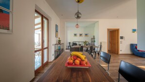 Ein Essbereich mit Holztisch, Obstschale, Stühlen und Blick in einen Speisesaal.