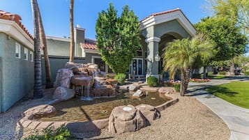 A residential area with a landscaped garden featuring a small waterfall, palm trees, and a well-maintained lawn.