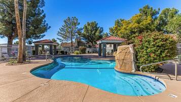 A swimming pool with a curved edge, a gazebo, and a rock feature.