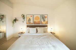 Ein Schlafzimmer mit einem Bett, Nachttischen, einem Spiegel und an Wänden befestigten Regalen mit Pflanzen.
