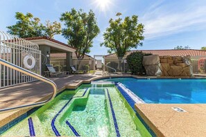 Ein Schwimmbecken mit gefliestem Sonnendeck, Liegestühlen und einem überdachten Bereich mit roten Dachziegeln.
