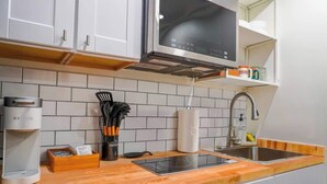 Une cuisine avec des armoires blanches, une hotte de cuisinière en acier inoxydable, un four à micro-ondes encastré, une machine à café et un évier.